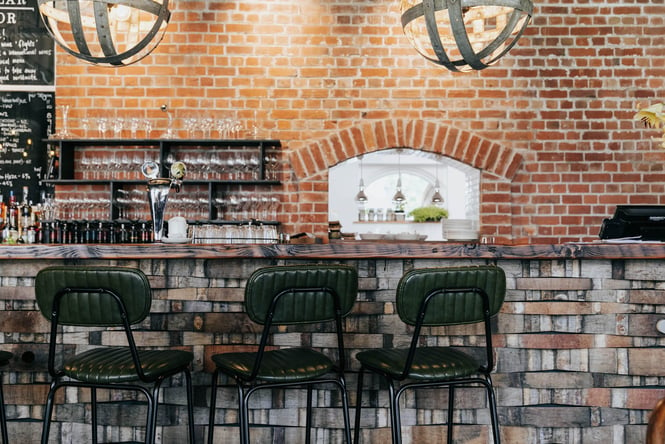 Exposed brick interior of Cellar Door in Christchurch with three green leather stools by the bar