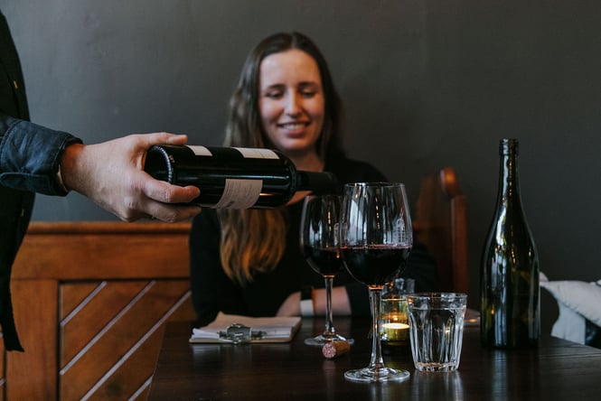 Diner sitting at table while waitstaff pours bottle of red wine into two glasses