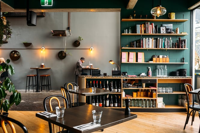 Interior of Mr Pickles in Hamilton with shelves filled with books and wine, and plants scattered around the floor and walls