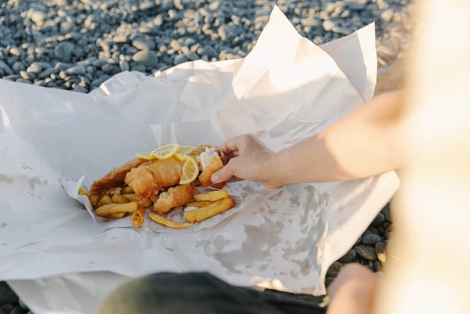 A hand reaching for fish and chips in paper.