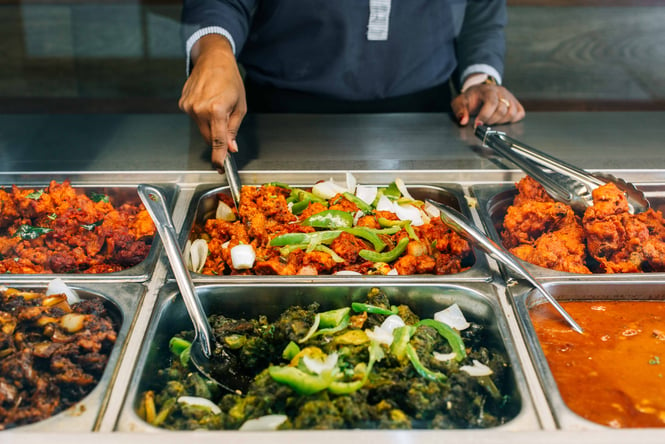 A close up of a hand scooping out some food from an Indian buffet.