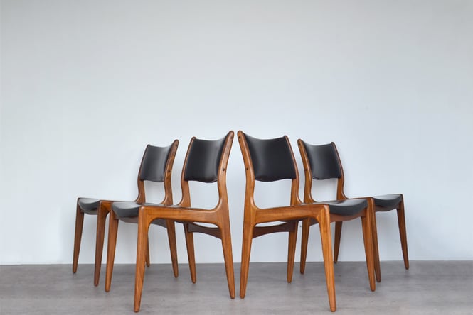 Four wooden chairs with black leather are on display.