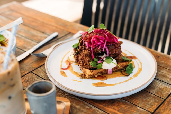 Fried chicken on waffles on a plate with bright pink pickled onions coriander and maple syrup dressing