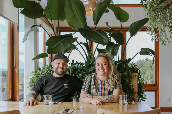 Yanina and Pablo smiling to camera under potted plants on a sunny day inside their restaurant Del Mar.