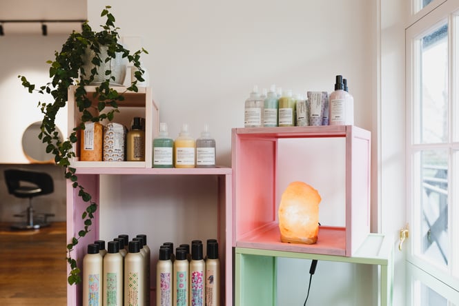 Hair salon products on a shelf next to orange crystal lamp in hair salon