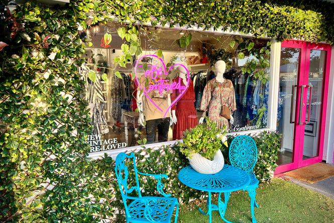 Looking into a window of a clothing store surrounded by bright green vines.