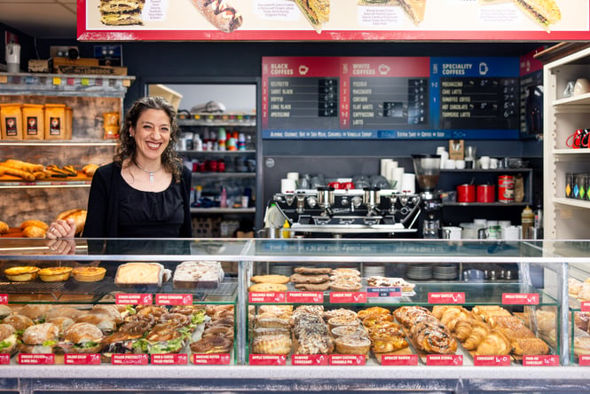 Woman smiles at the camera from behind the cabinet filled with baked goods and sandwiches at Ciabatta.