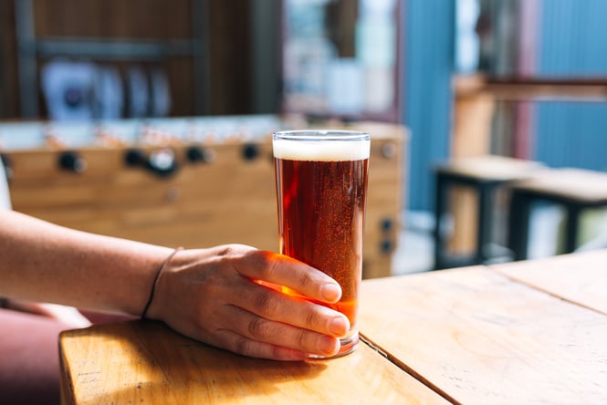 A close up of a hand holding a glass of beer.