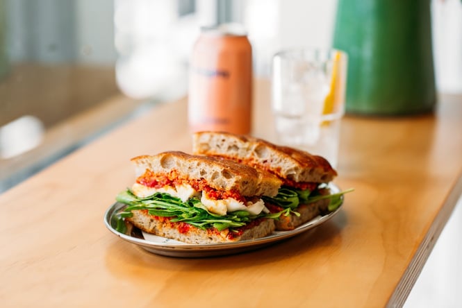 A focaccia sandwich with red pesto, mozzarella and greens on a plate at Fred's.