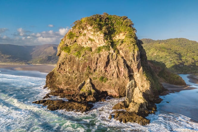 Looking down on Piha beach and its large cliff and green surroundings