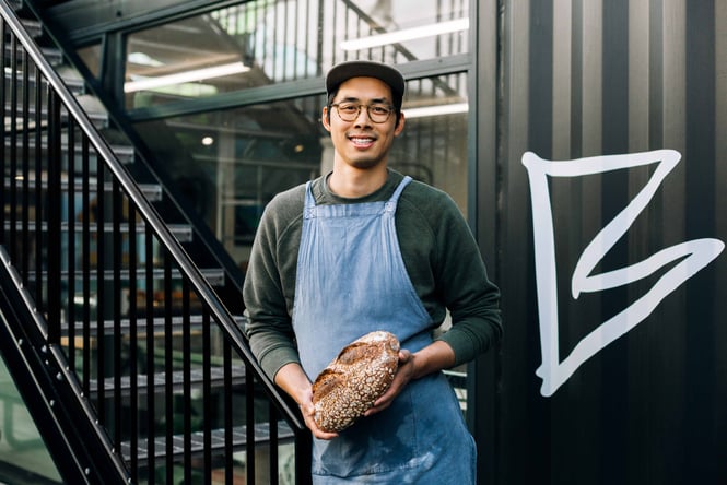 A man holding a loaf of bread smiling to camera.