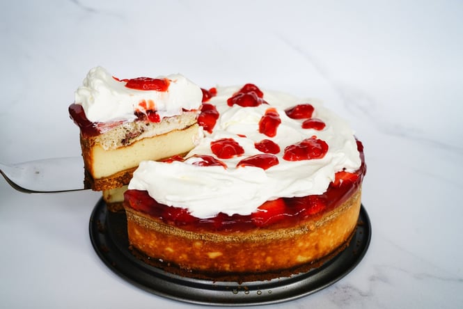 A white and red cake being sliced on a white table.