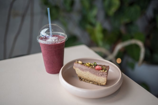 A vegan slice on a table sitting next to a berry smoothie.