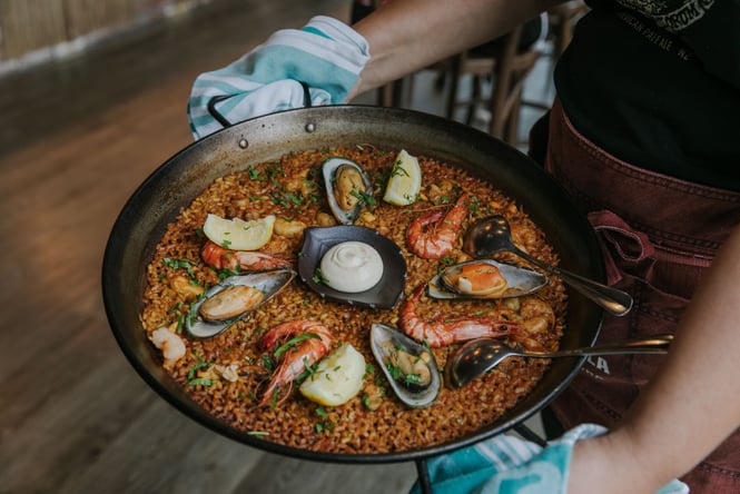 A person holding a pan of paella.