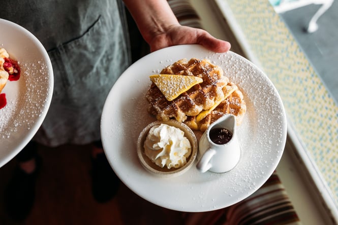 A hand holding a plate of waffles.