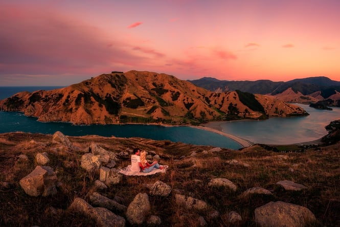 A couple sitting watch the sunset over Cable Bay in Nelson Tasman.