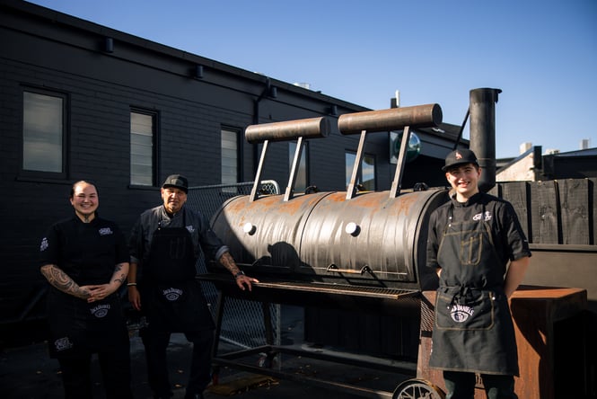 Chefs standing outside a smoker.