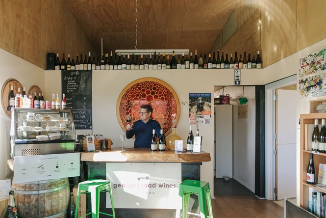 A man holding a glass of wine behind a counter inside a cellar door.