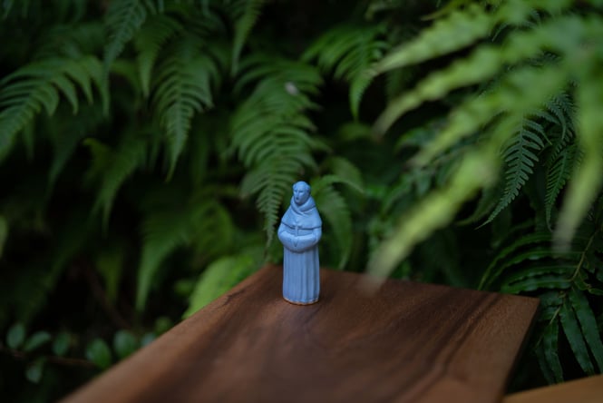 A blue chess piece sitting in front of a bush.