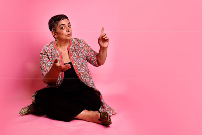 A woman sitting on the ground in front of a pink background.