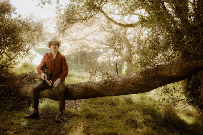 A man dressed as a cowboy sitting on a tree branch.