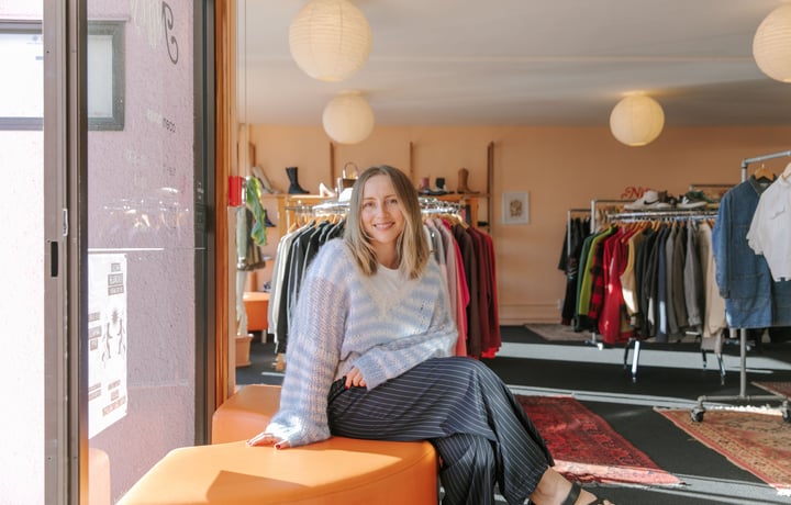 Photo of Rosie Carroll sitting on orange semi-circle couch at her secondshop Nifty in Christchurch
