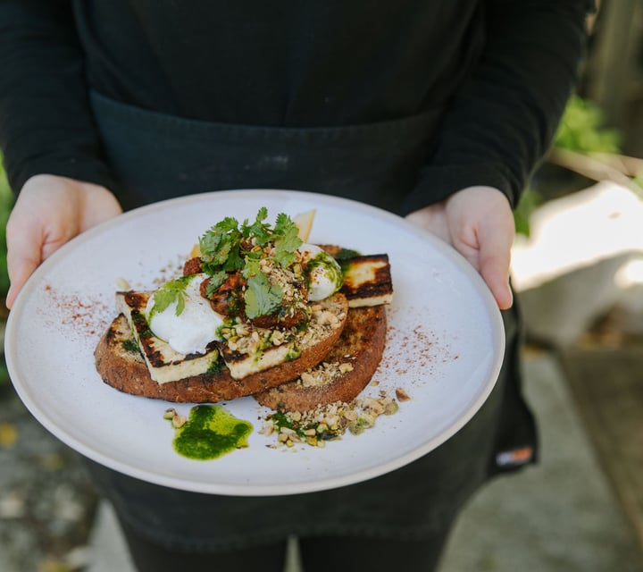 Person holding a plate of halloumi and poached eggs from Deville, Nelson.