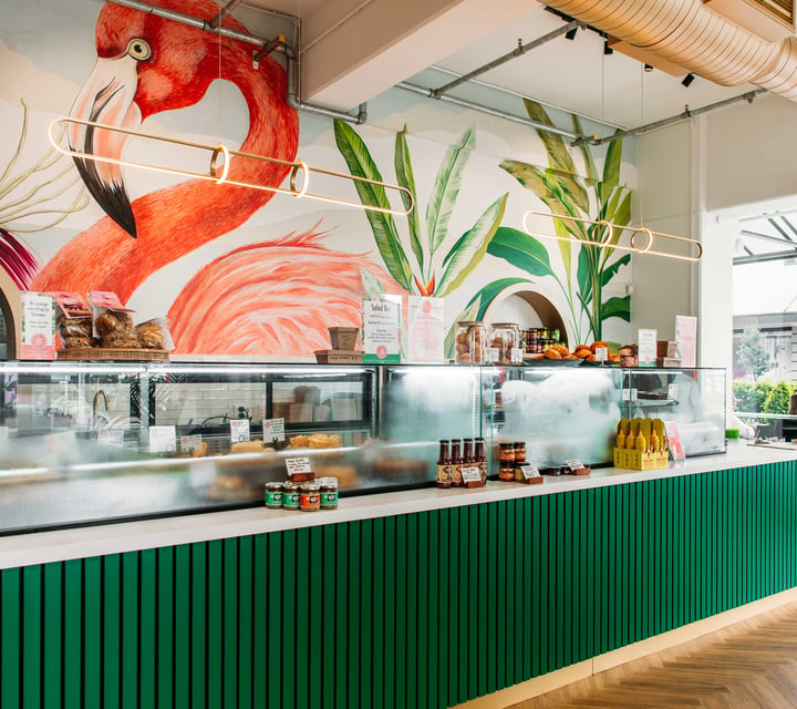 The green counter inside Long Island Delicatessen with a backdrop of a flamingo painted on the wall.