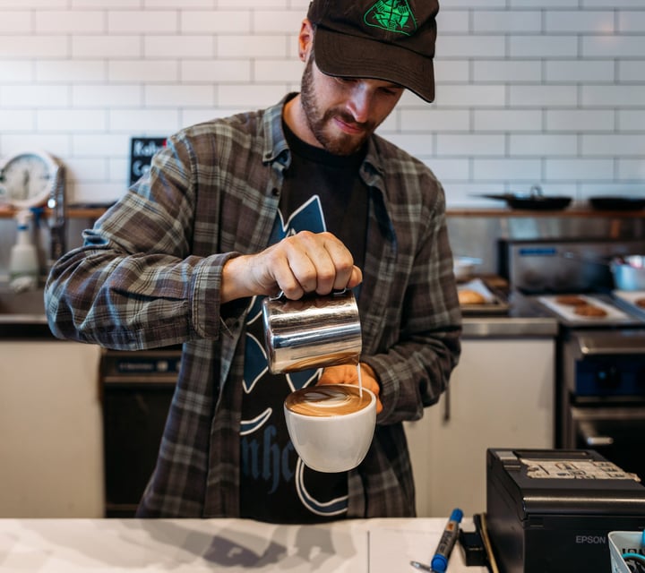 Barista pouring milk into freshly made coffee at cafe