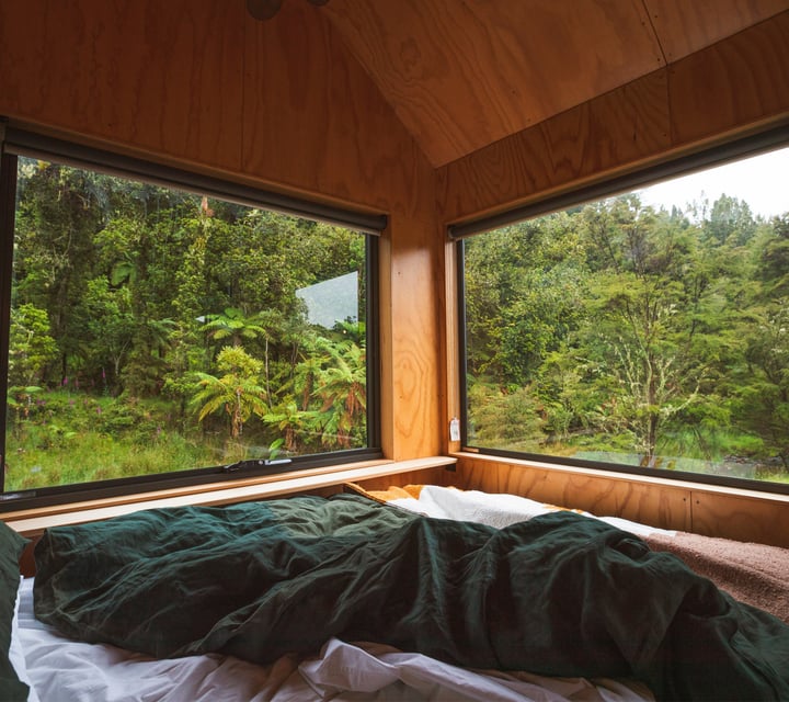 A cosy looking bed next to a window in a cabin.