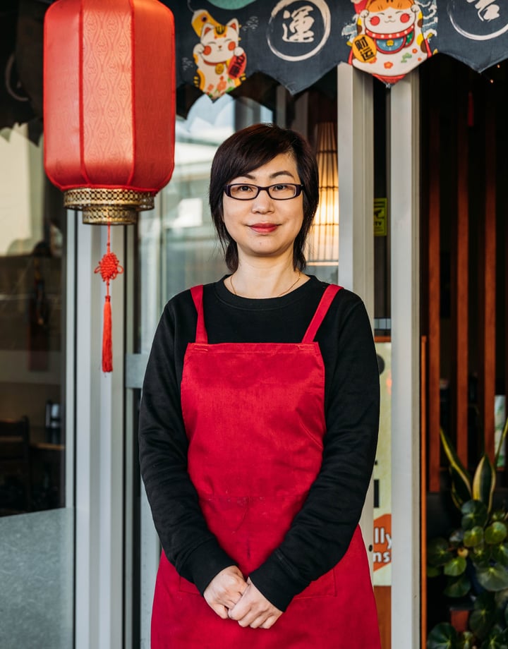A woman dressed in red and black standing outside a Chinese restaurant smiling to camera.