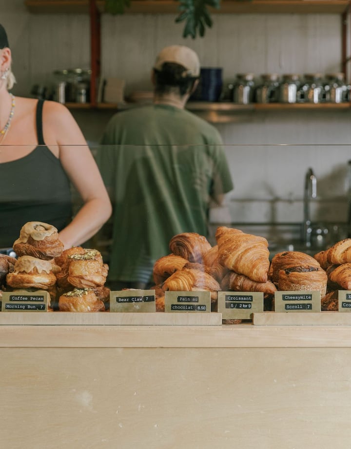 Three staff members behind the counter at Grizzly, with a cabinet filled with croissants, morning buns and filled bagels