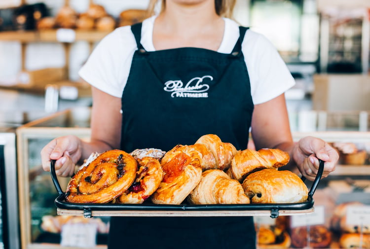 A staff member holding tray of freshly baked pastries.