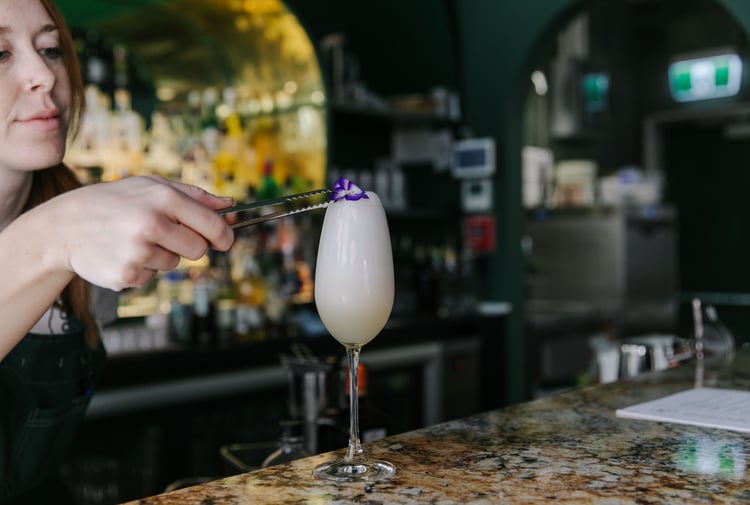 Bartender adding purple pansy as a garnish on top of a cocktail