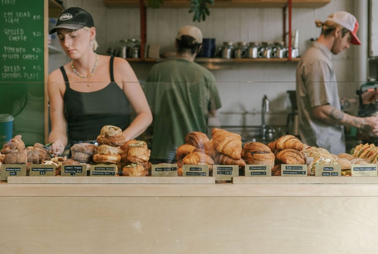Three staff members behind the counter at Grizzly, with a cabinet filled with croissants, morning buns and filled bagels