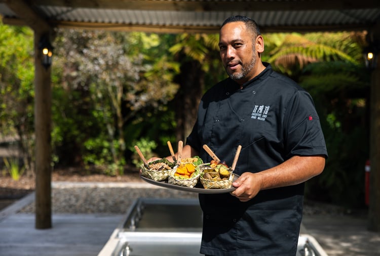 A man wearing a chef's outfit holding a tray of Maori food.
