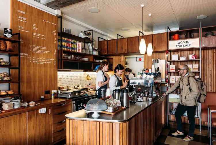 A customer and baristas standing inside the timber-lined Customs coffee shop.