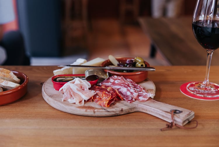 A glass of red wine next to a platter of cheese and cured meats at Salut Salut.