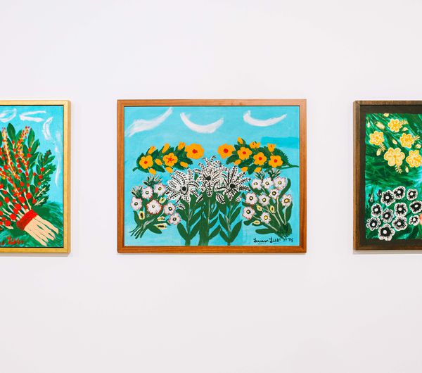 A close up of three brightly coloured artworks of flowers on a white wall inside Govett Brewster Art Gallery.