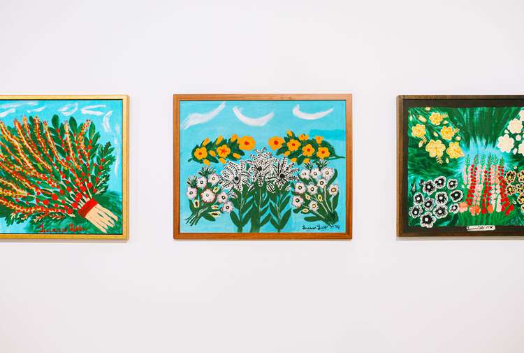 A close up of three brightly coloured artworks of flowers on a white wall inside Govett Brewster Art Gallery.