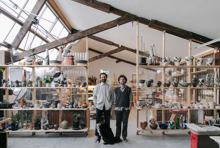 Jamie Smith and Tom Baker of Kiln Studio standing in their studio with a black dog.