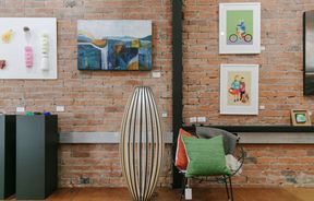 Art on display on a brick wall and a colourful chair on a wooden floor at 77 Art + Living in Fairlie.