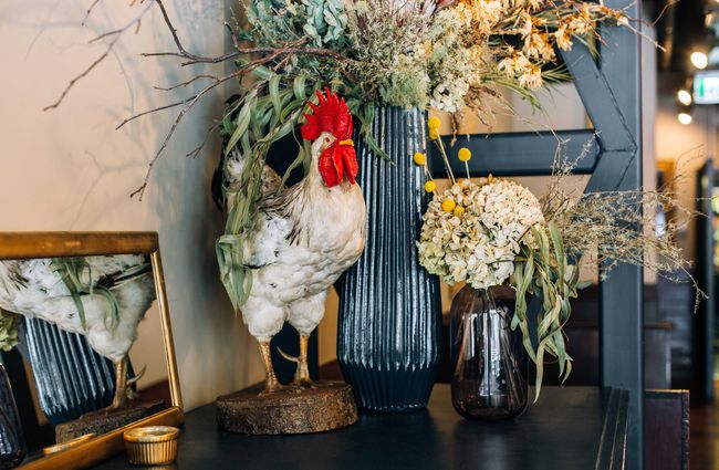 Taxidermy rooster with dried flowers on display.
