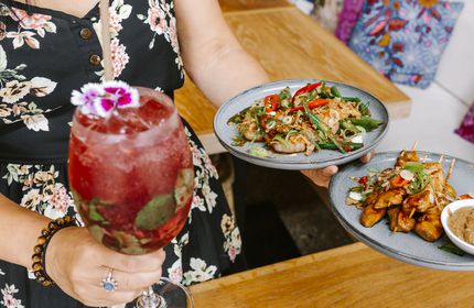 Woman holding cocktail and plates of food at Bandung Café, Auckland.