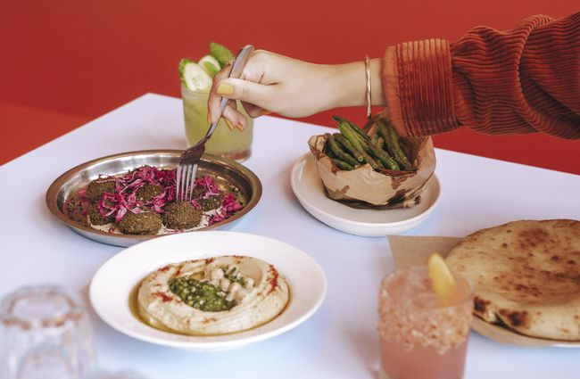 A hand holding a fork reaching for a piece of falafel on a plate.