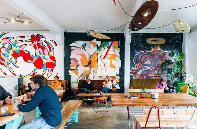 People enjoying coffee on the vintage couches with artwork behind them at Escape Coffee Roasters, New Plymouth.