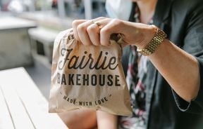Close up of a woman holding a paper bag with 'Fairlie Bakehouse' written on it.