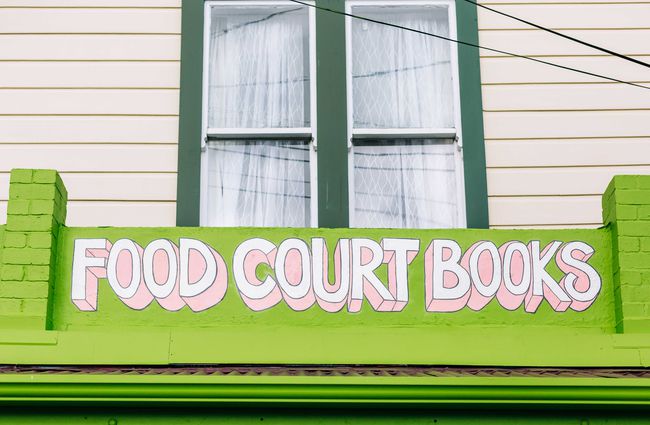 Close up of the pink and white sign painted on the front of the Food Court Books store front.