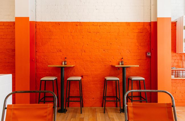Stools at leaner table against an orange wall at Fred's, Wellington.
