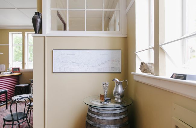 Wine barrel table with silver jug on top and a framed picture above at Vinters Drop in Kurow, Waitaki.